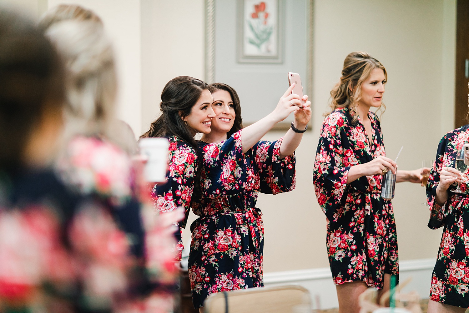 Bridesmaids taking a selfie as they prepare for the ceremony in their colorful floral robes 