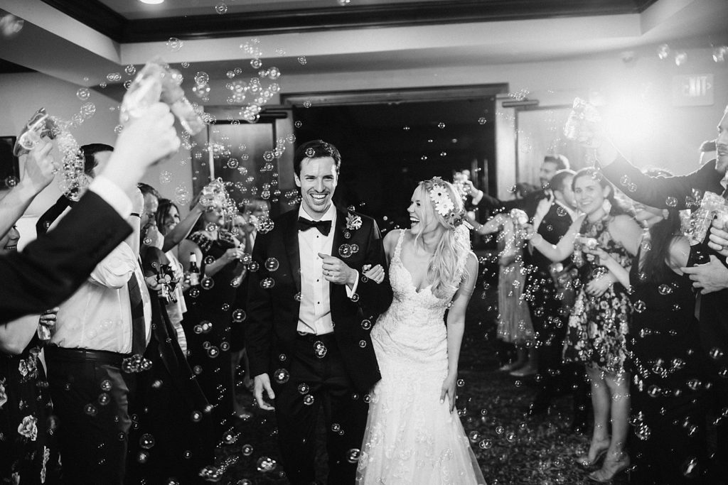 Black and white image of the bride and groom as they enter their reception room surrounded by bubbles 