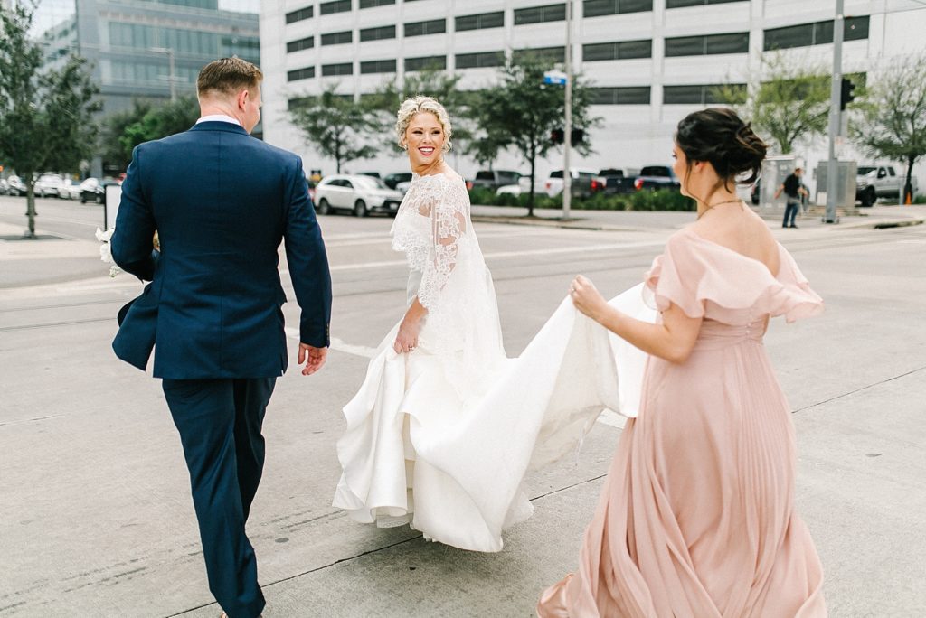 Bridesmaid hold dress for Bride as the Bride and Groom cross the street in Houston